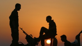 The sun sets as Israeli army soldiers stand on top of military vehicles just outside the Gaza Strip near Kibbutz Kfar Azza.